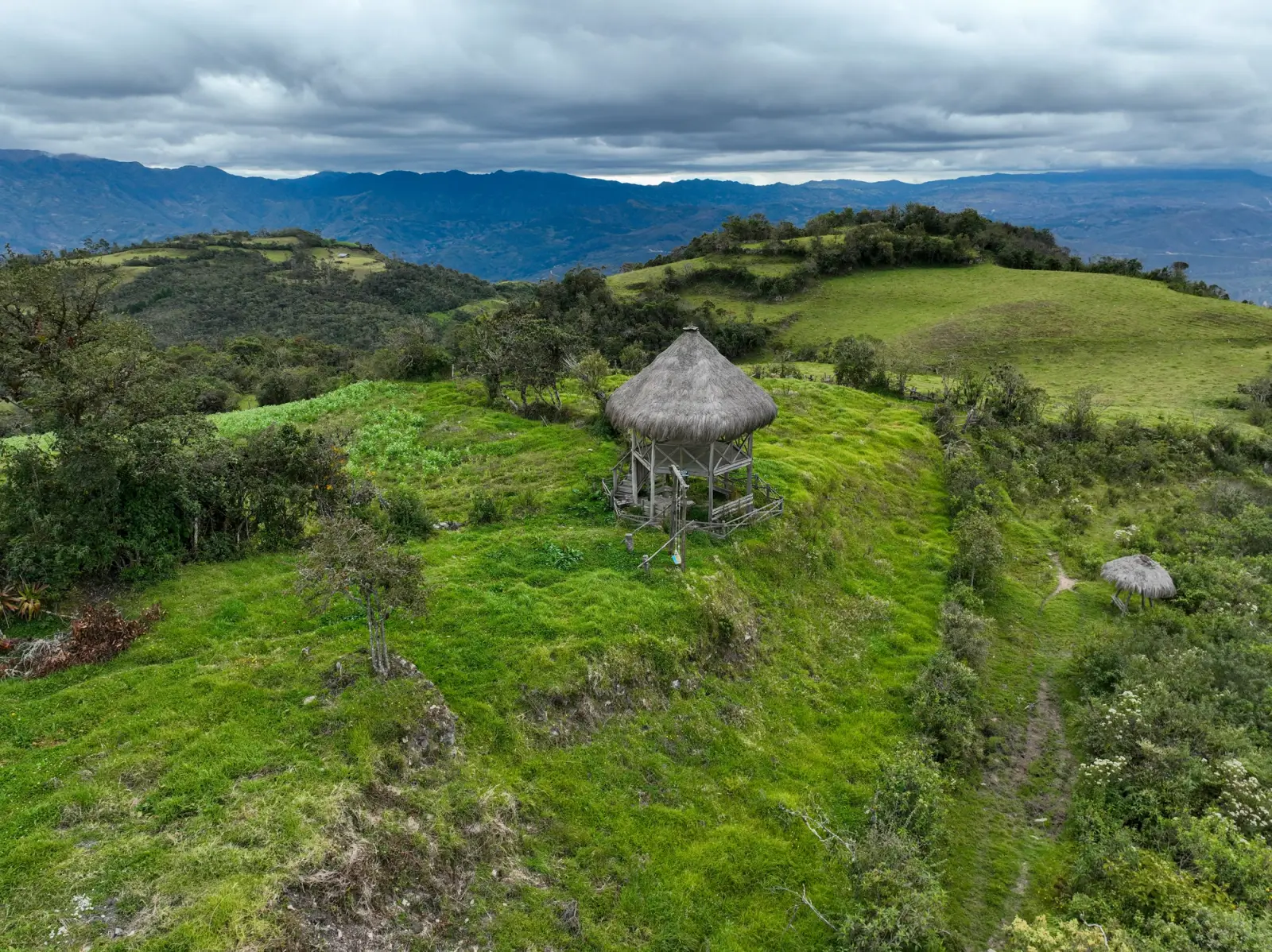 Mirador con techo de paja sobre una colina verde con montañas al fondo