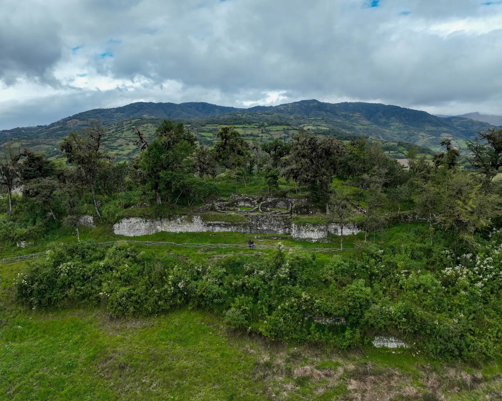 Muros de un sitio arqueológico entre árboles, con cerros al fondo