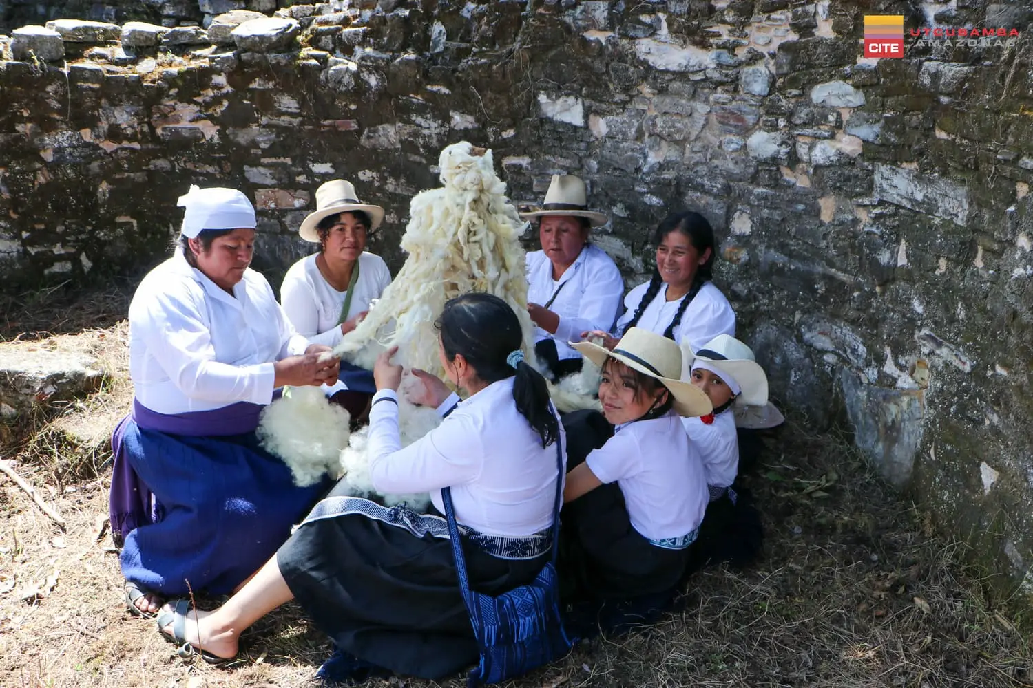 Artesanas y niñas abriendo lana cruda a mano, sentadas dentro de un recinto de piedra
