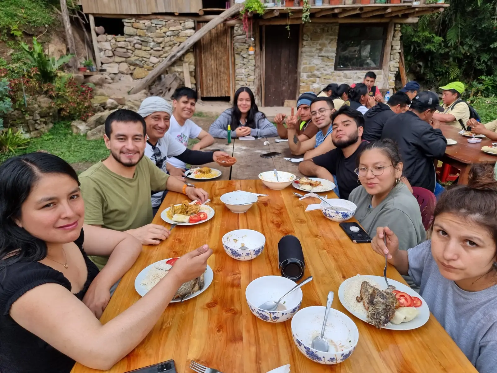 Grupo almorzando en una mesa larga de madera frente a una casa de piedra