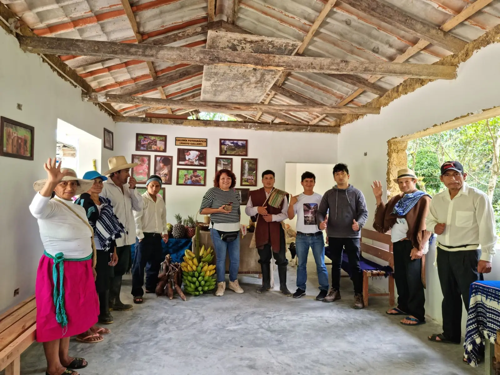 Grupo de personas saludando en una sala con galería fotográfica y racimos de plátano