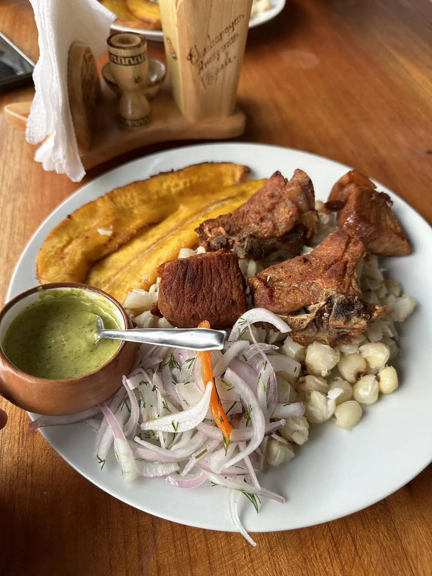 Plato de chancho frito con mote, plátano frito, salsa criolla y ají