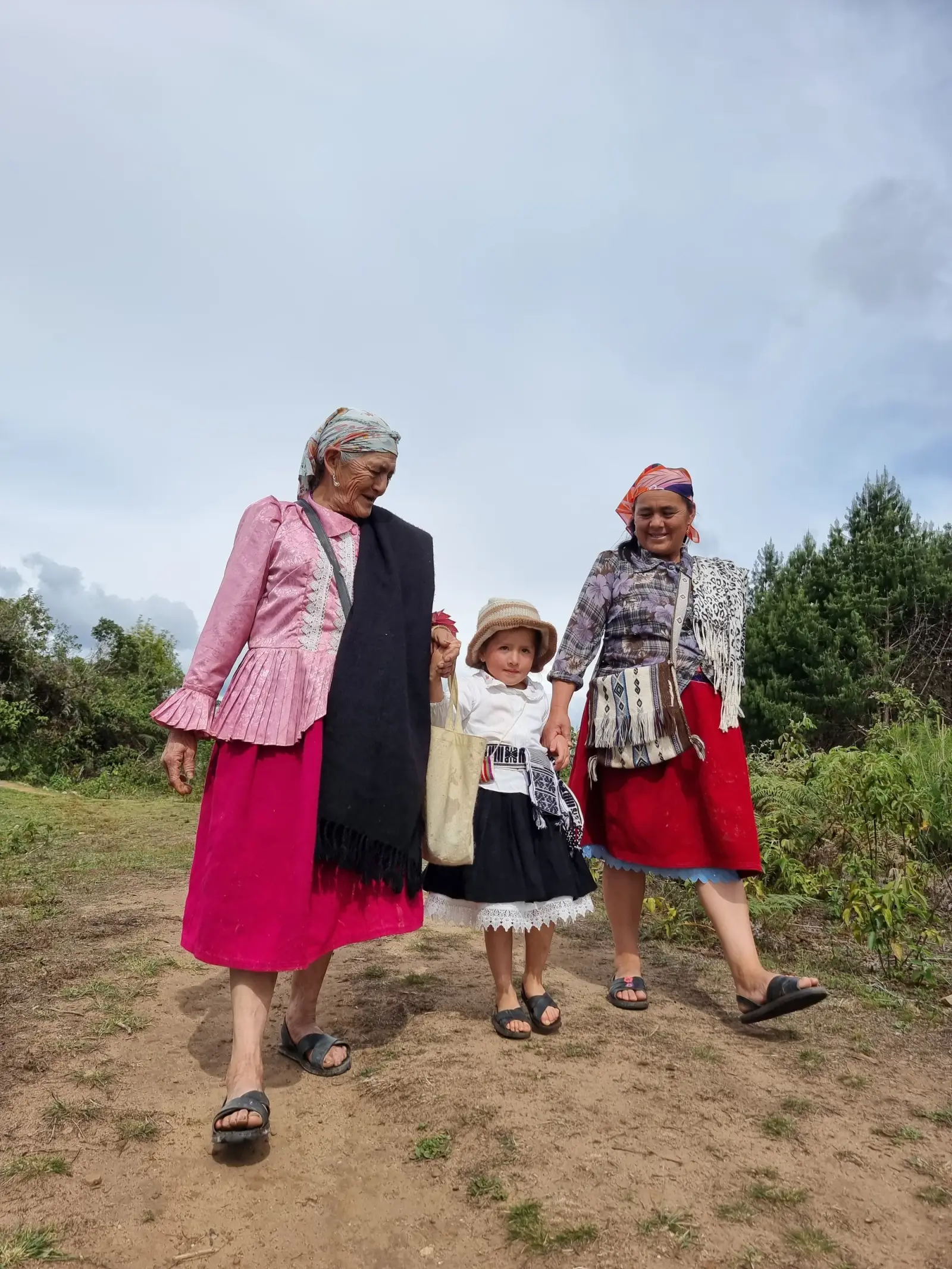 Dos mujeres con ropa tradicional caminan de la mano con una niña por un sendero