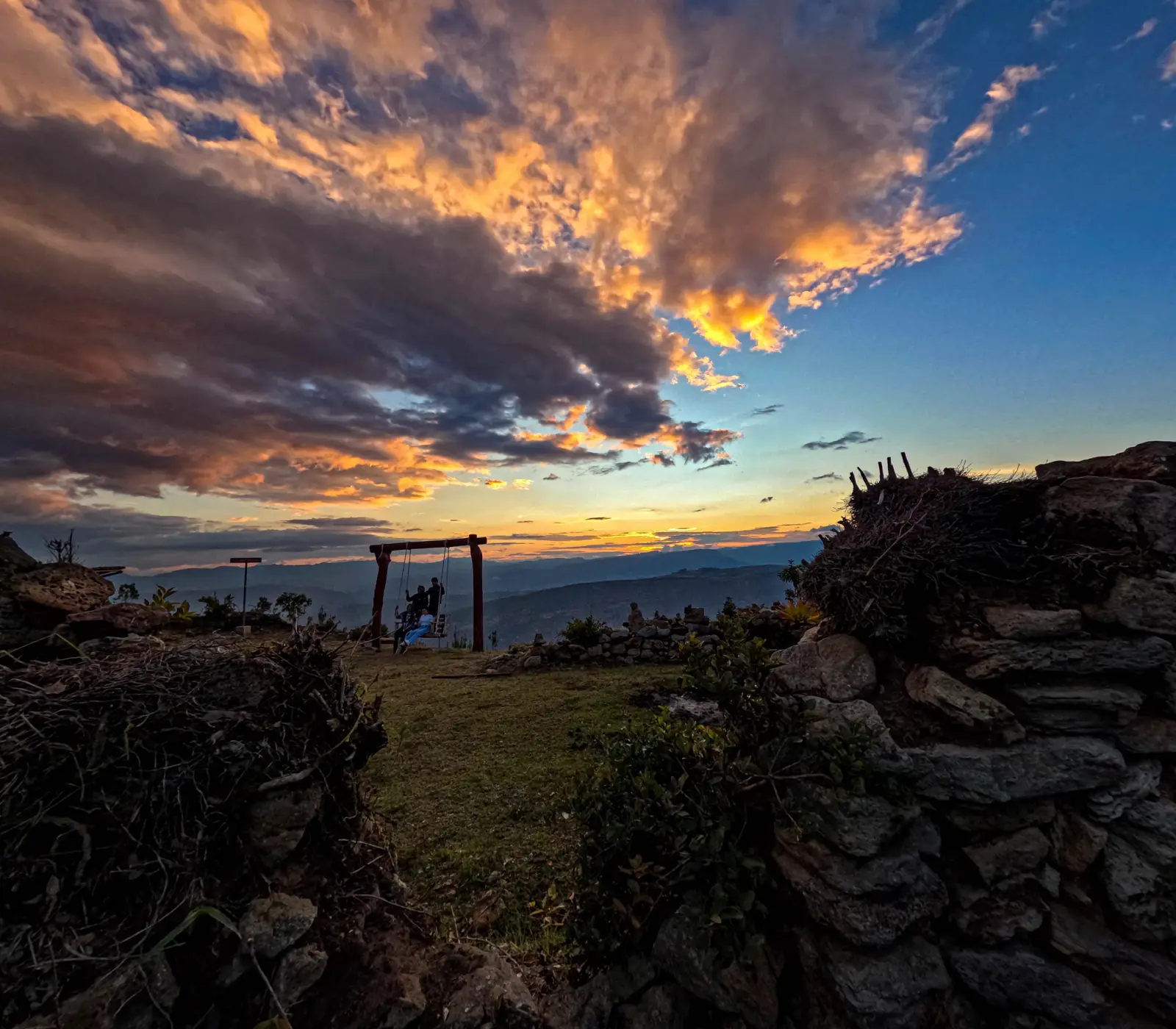 Atardecer sobre las montañas con un columpio de madera entre muros de piedra