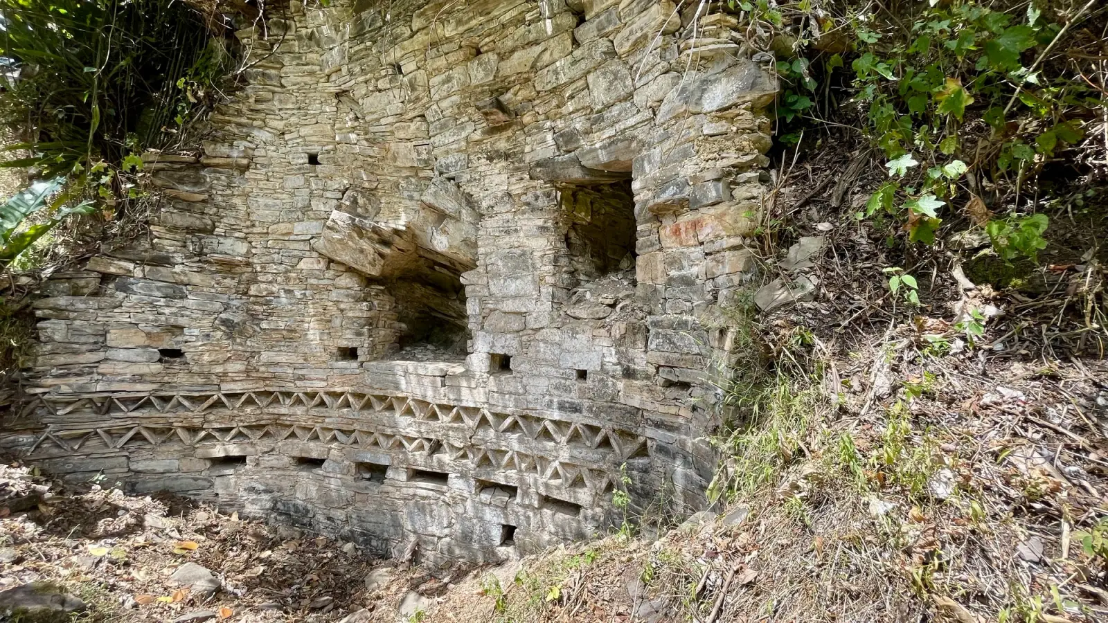 Muro de piedra con frisos en zigzag y nichos bajo un alero rocoso