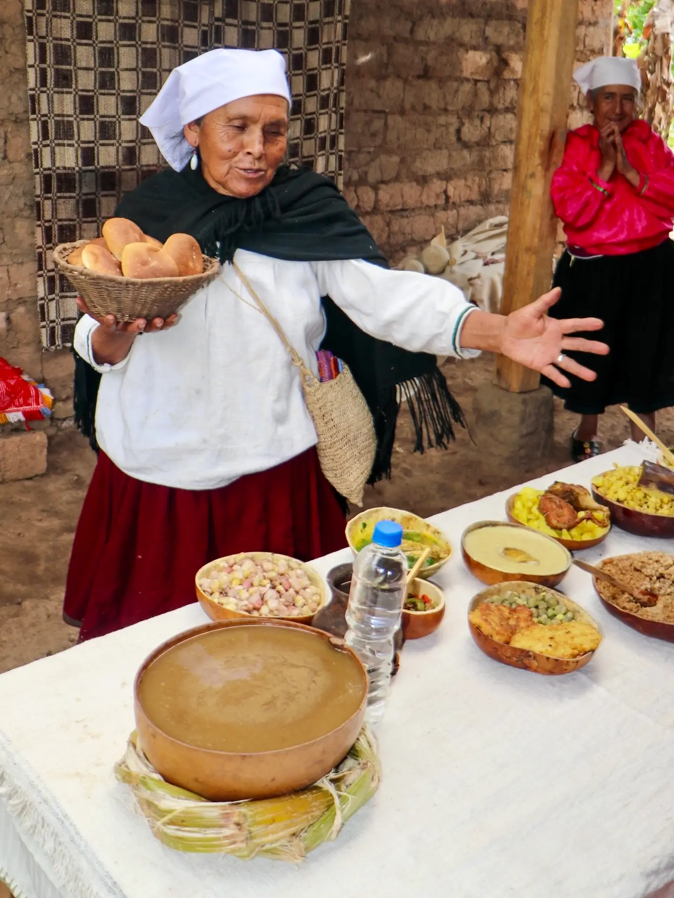 Mujer con canasta de panes presenta una mesa de platos típicos en mates