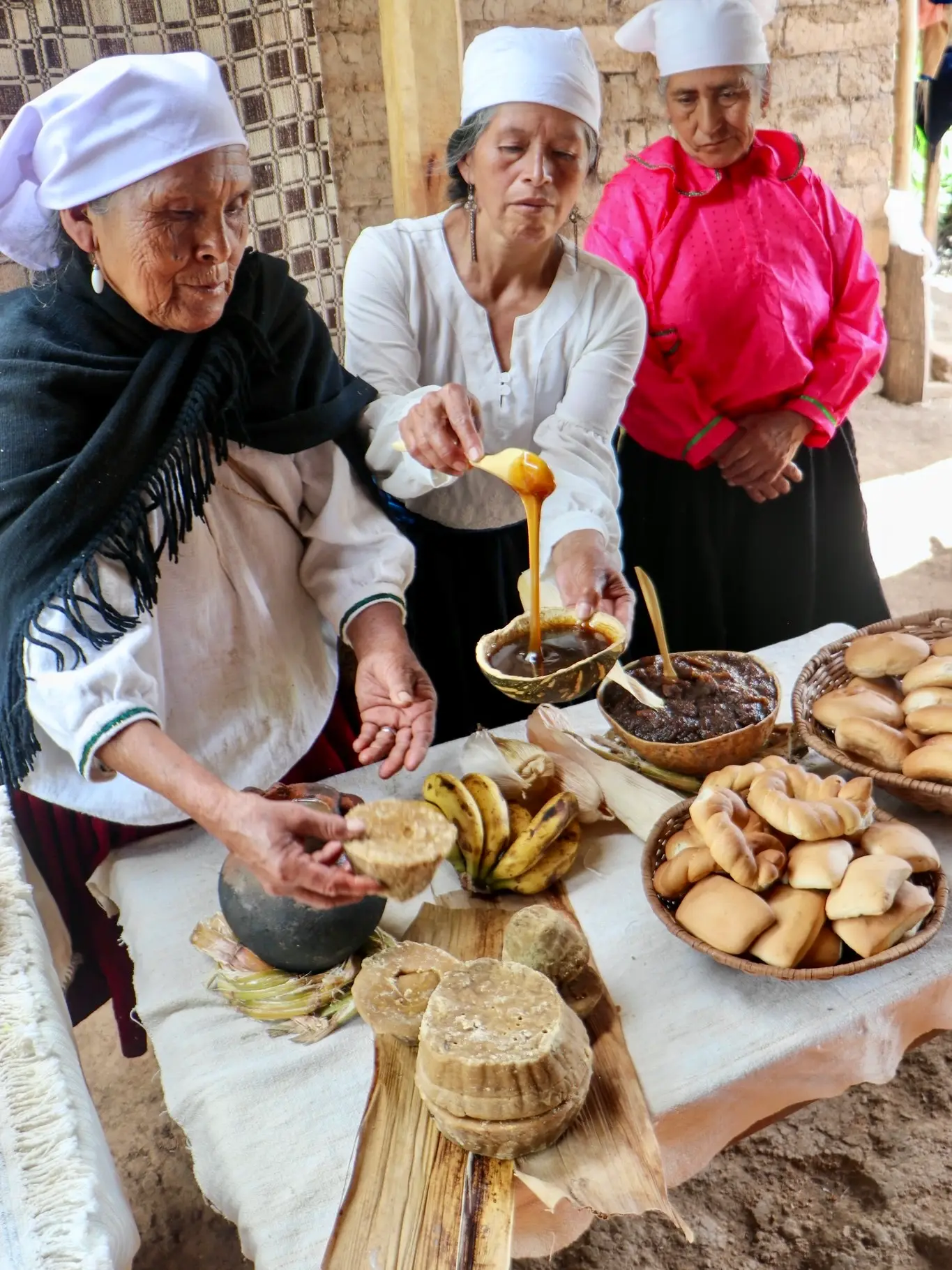 Mujeres sirven miel de caña en una mesa con chancaca, plátanos y panes
