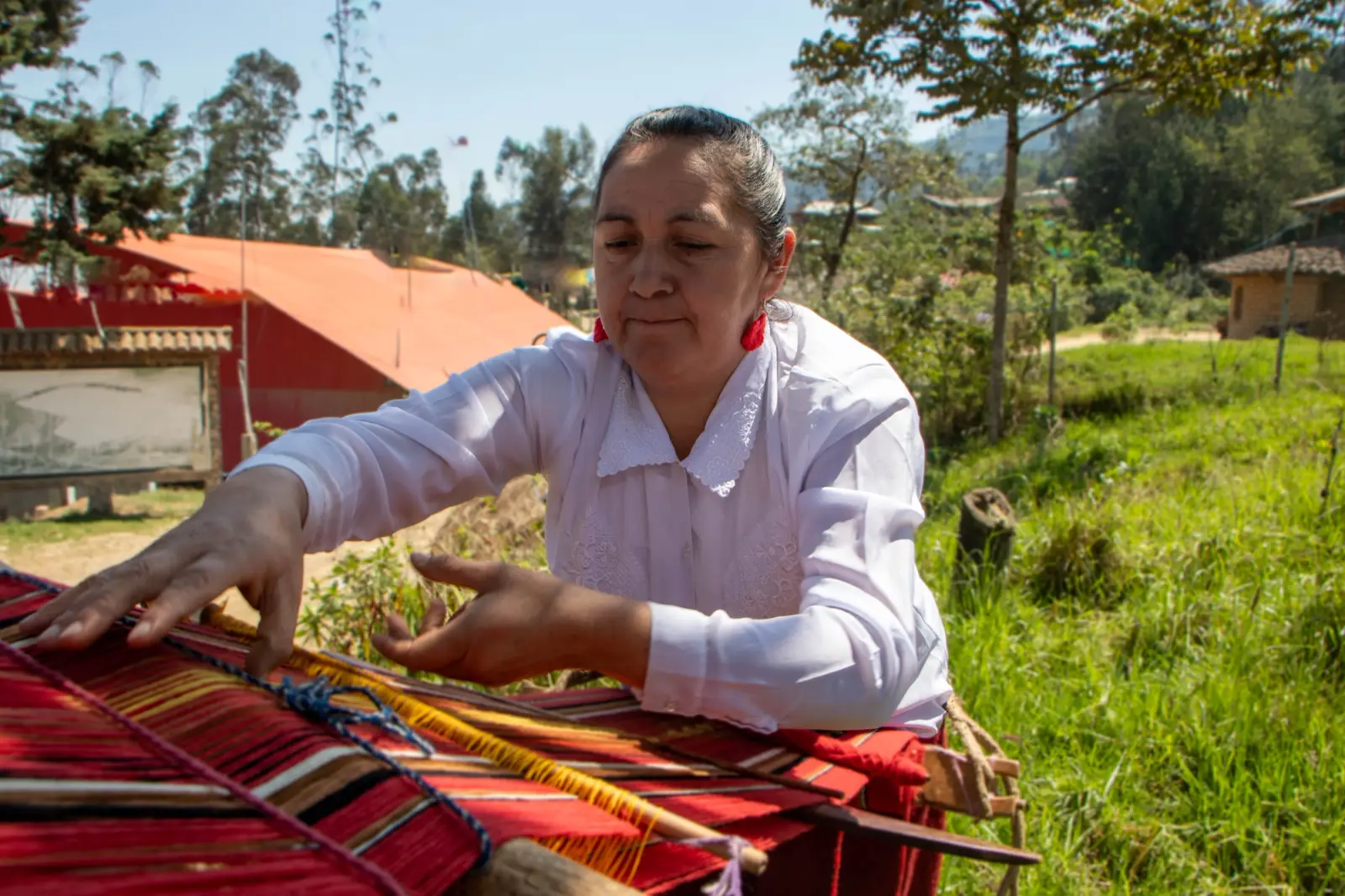 Artesana tejiendo una manta roja en telar de cintura al aire libre