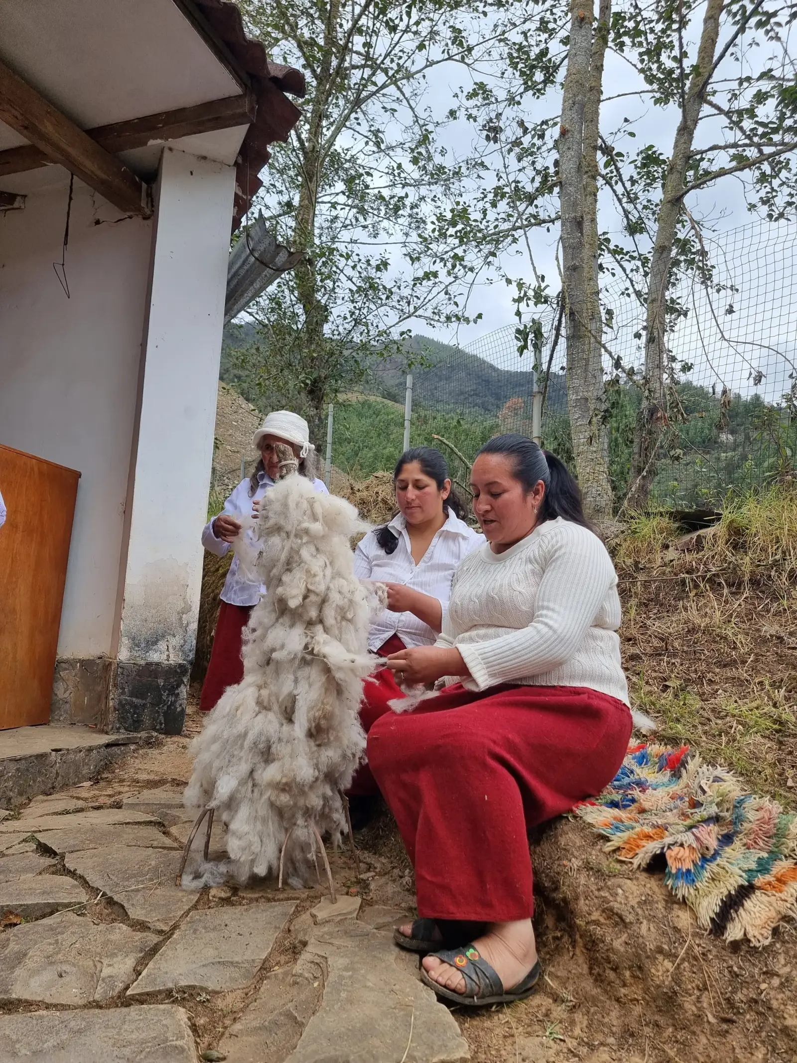 Artesanas habilitando la lana de oveja, el tishar, junto a una vivienda