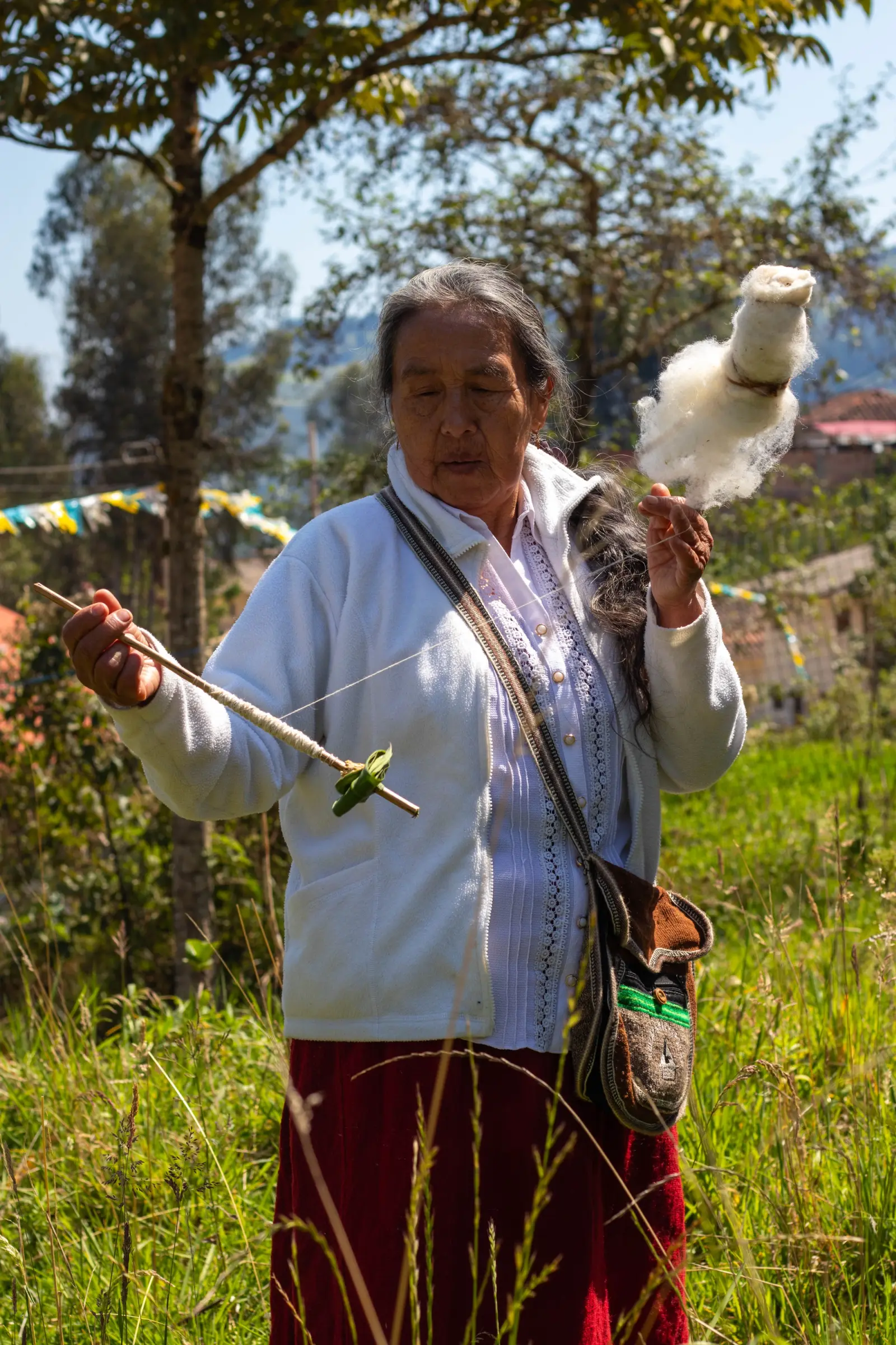 Artesana hilando lana de oveja con pushcana entre pastizales