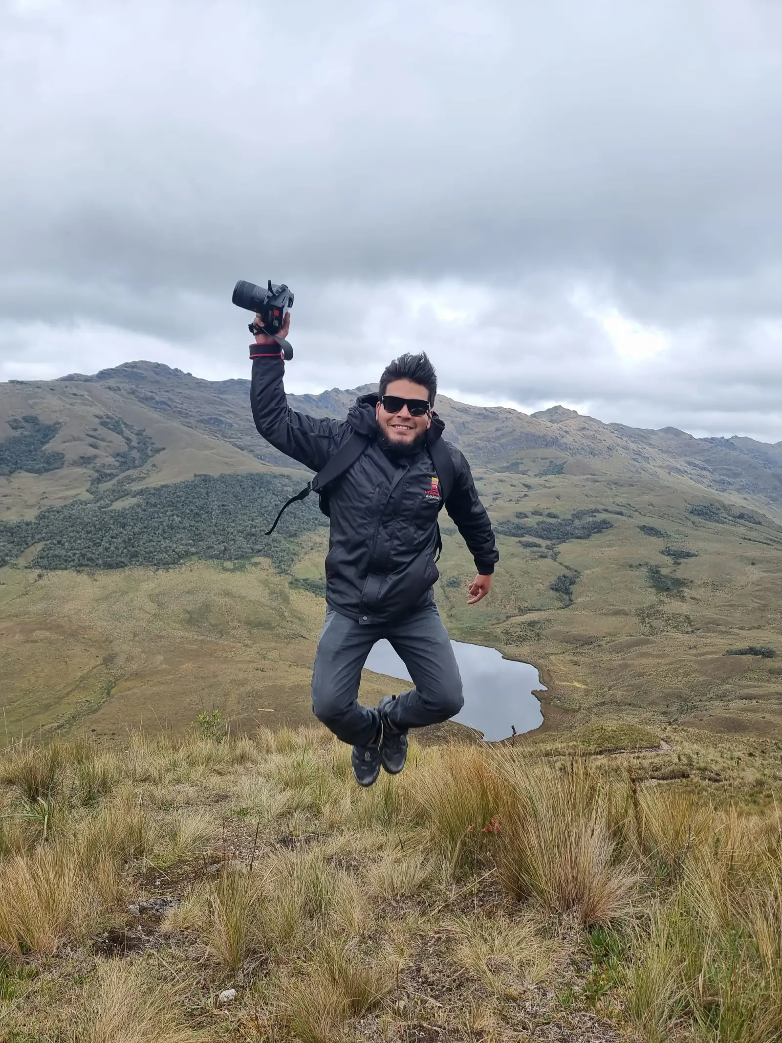 Visitante saltando con una cámara en la puna, con la laguna Cuchacuella detrás