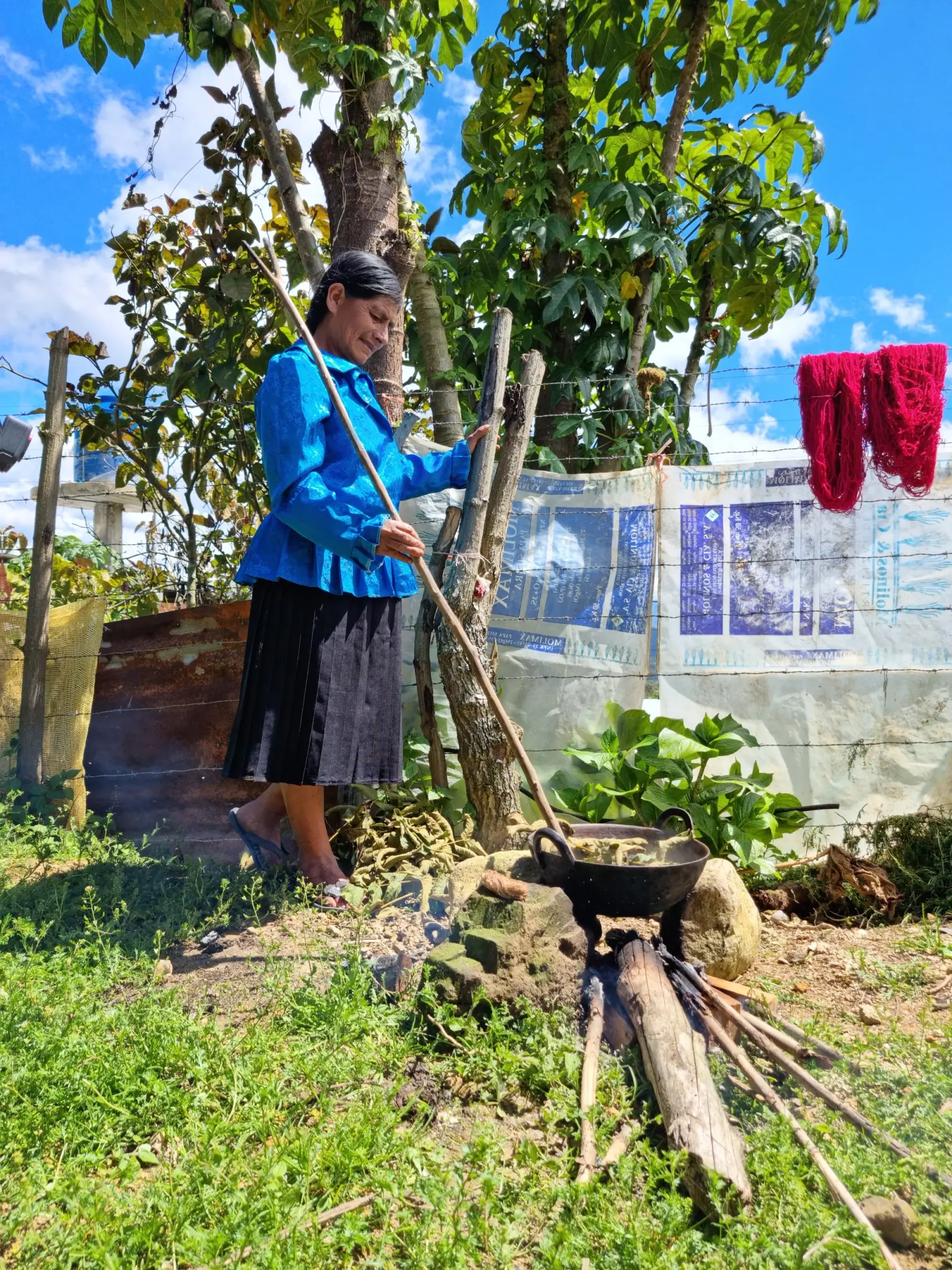 Artesana removiendo una paila de tinte natural al fuego junto a madejas rojas