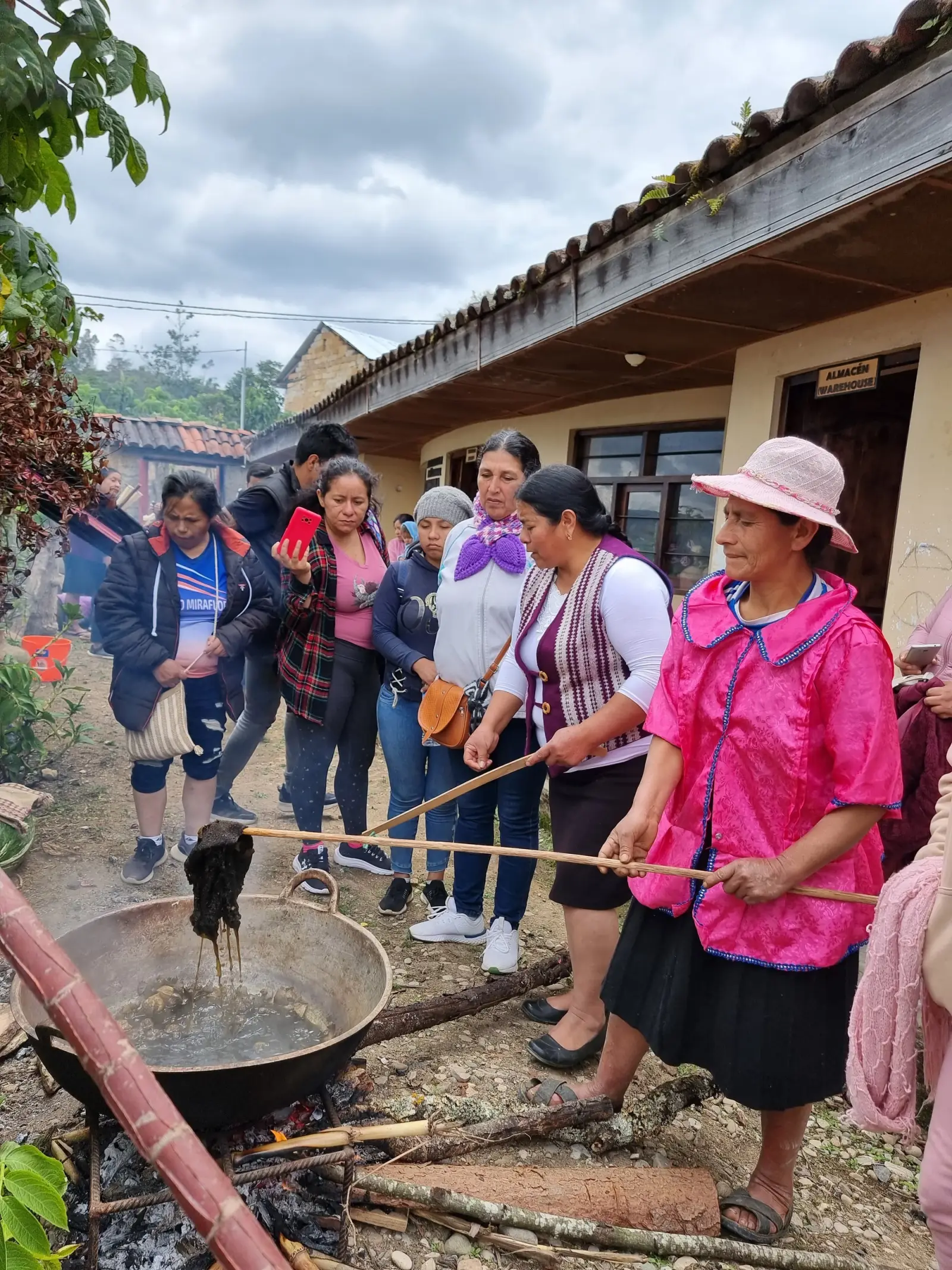 Artesanas sacando lana teñida de una paila al fuego frente a visitantes